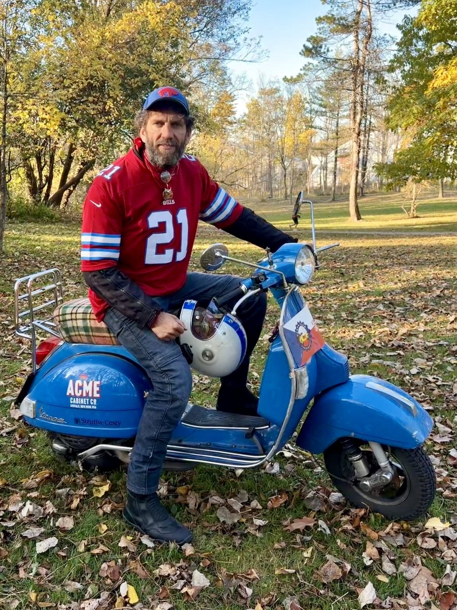 Lou in a red Bills number 21 jersey on Adina, his blue Vespa, in an autumn park in Buffalo